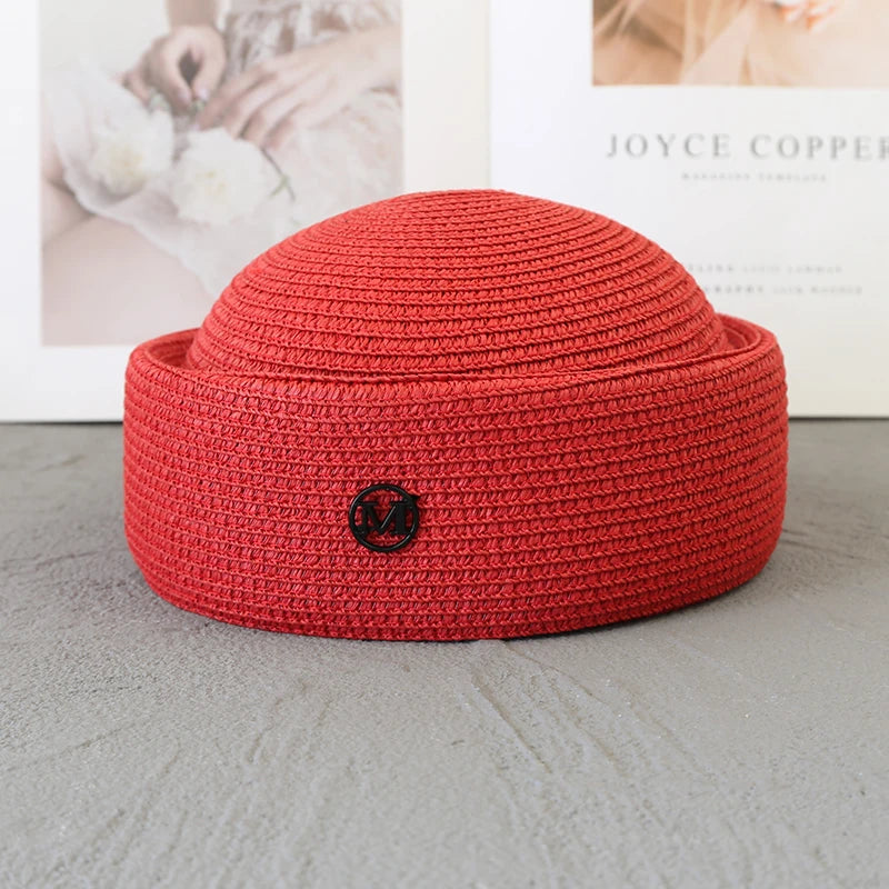 A terracotta red straw pillbox sun hat with a woven texture resting on a gray surface.
