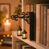 A black wrought iron lantern shelf lamp hangs on a white shelf next to a row of old books.