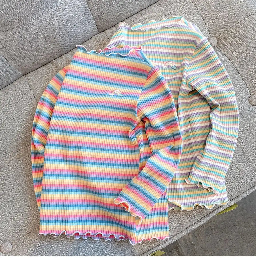 A long-sleeved striped shirt featuring a rainbow of colors and a flower print on a light gray background.