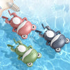 Three bath toys shaped like ducks and penguins in pink, gray, and green floating in clear water.