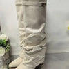 A pair of beige knee-high boots with a chunky heel and a metal buckle displayed against a white background.