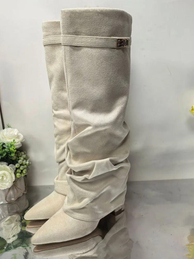 A pair of beige knee-high boots with a chunky heel and a metal buckle displayed against a white background.