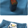A small black electronic device is placed on a blue fabric, next to a pair of blue kids' beach shorts.