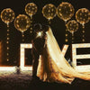 A couple is embraced under a canopy of glowing LED light-up balloons at night.