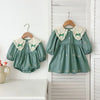 A teal kids princess dress with floral embroidery and lace trim hanging on a wooden hanger against a white background.