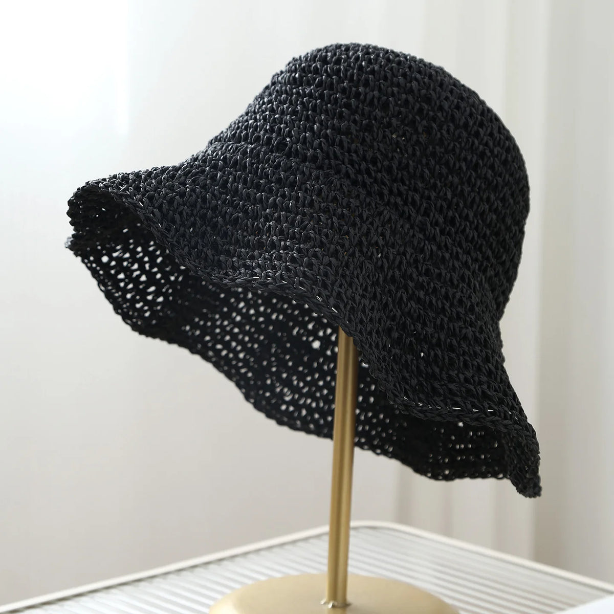 A black crochet fisherman hat with a wide brim displayed on a stand.