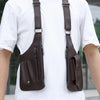 Vista cercana de un bolso táctico cruzado marrón oscuro para hombre con correas dobles, usado sobre camiseta blanca.
