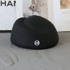 A black knitted sun hat with a wide brim and a silver logo resting on a gray surface.