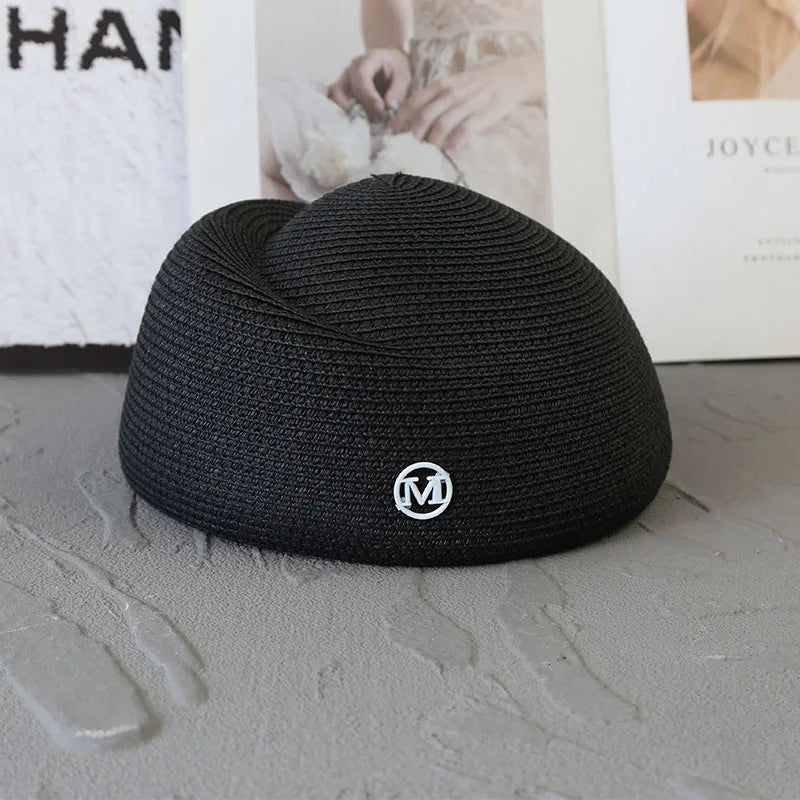 A black knitted sun hat with a wide brim and a silver logo resting on a gray surface.