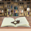 Un libro abierto con un marcapáginas de madera con forma de gato y perro sobre una mesa de madera, con estanterías al fondo.