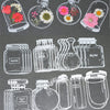 A collection of transparent glass bottles and jars filled with dried flowers and various liquids, used as DIY bookmarks.