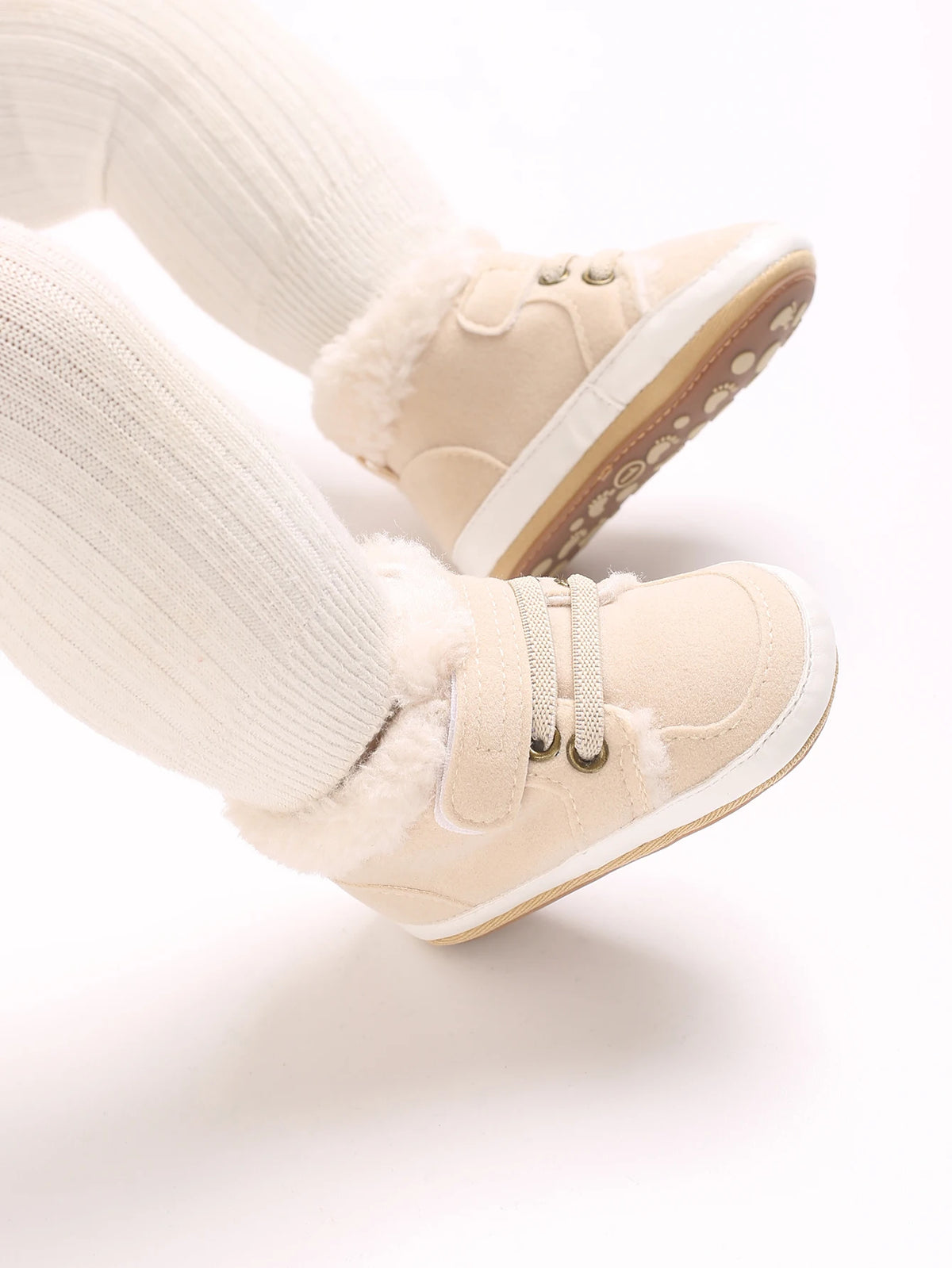 A pair of beige soft cotton baby winter snow boots with fuzzy trim and white socks.