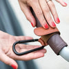 A hand is adjusting adjustable leather stroller hooks for diaper bags and shopping.