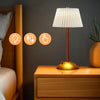 A modern table lamp with a white fabric shade and gold base sits on a wooden nightstand.