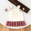 A white kids summer pinafore dress with red trim and a strawberry and bunny print, displayed on a wooden board.