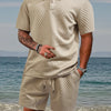 A man wearing a beige jacquard short-sleeve shirt and drawstring shorts set standing near the water.