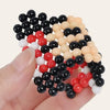 A hand holds a pile of 300 colorful water beads in various shades of black, red, white, and beige.
