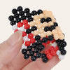 A hand holds a pile of 300 colorful water beads in various shades of black, red, white, and beige.