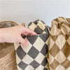 A hand is holding up a pair of beige and black checkered cotton harem pants with pockets.