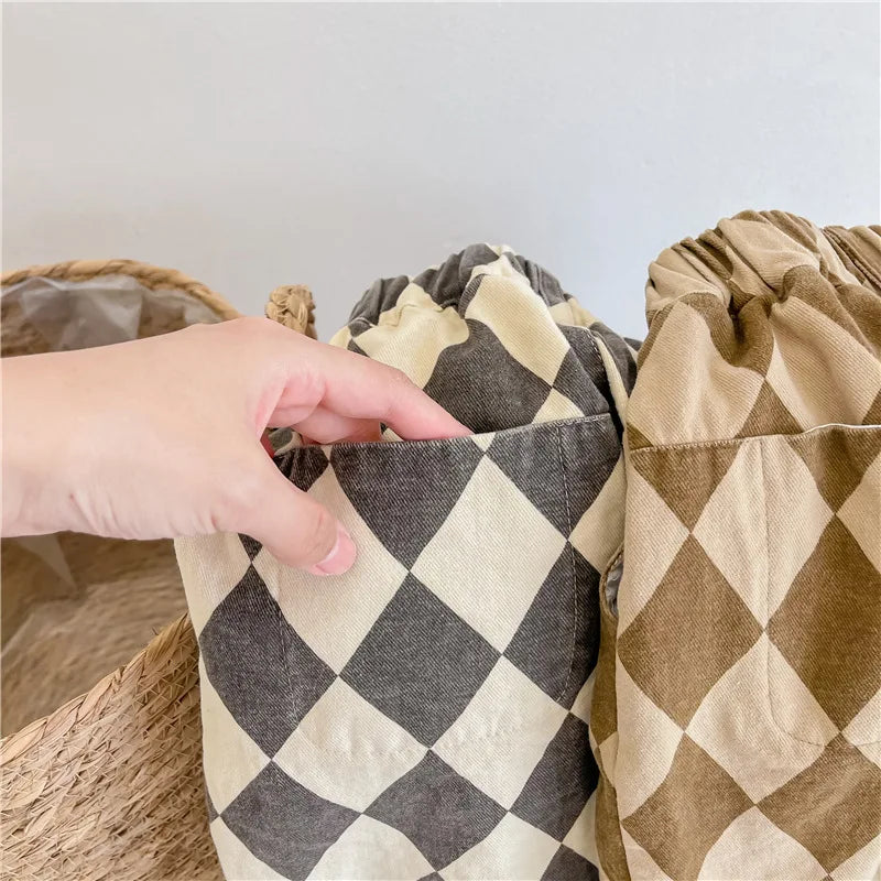 A hand is holding up a pair of beige and black checkered cotton harem pants with pockets.