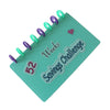 A green binder with 52 purple and green pins, labeled Savings Challenge Weeks.