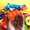 A hand holds an orange marble run building block piece amidst various colorful plastic tracks and blocks.