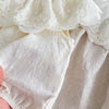 A close-up of a white baby girl jumpsuit featuring a delicate lace collar and textured cotton fabric.
