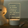 A white acrylic message board lamp displays a handwritten message on a clear panel.