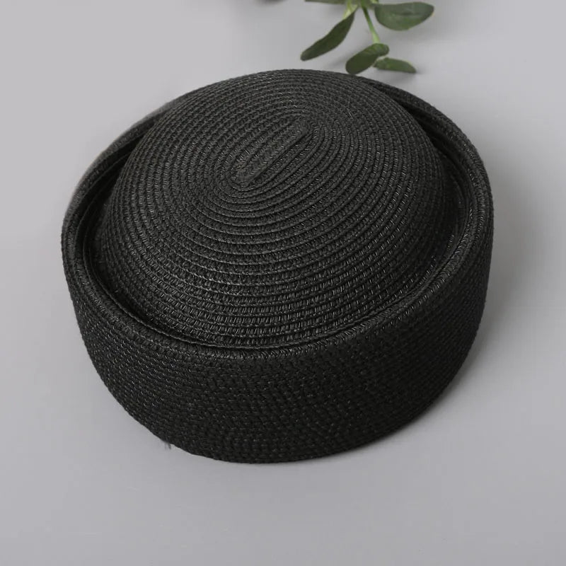 A black woven straw pillbox sun hat with a wide brim shown against a light gray background.