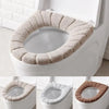 A beige soft acrylic toilet seat cover is shown being placed on a white toilet bowl.