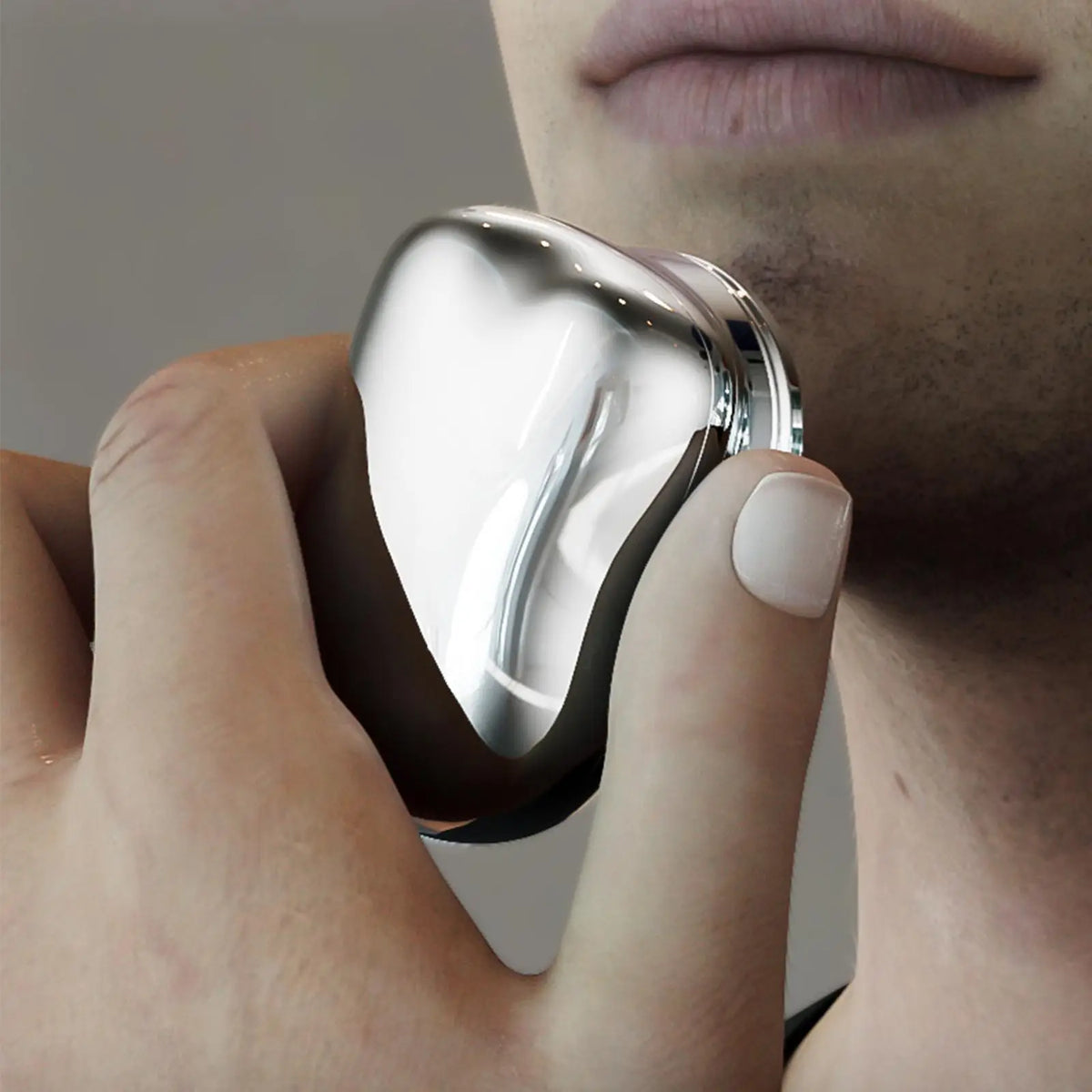 A hand holds a silver electric shaver, showing the device's design and texture.