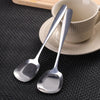 A pair of shiny stainless steel serving spoons resting on a saucer next to a cup.