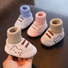 A hand holds a pair of soft-soled baby first walker booties in various pastel colors like light pink, blue, and beige.
