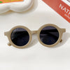 A pair of light beige sunglasses with dark lenses resting on a white surface.