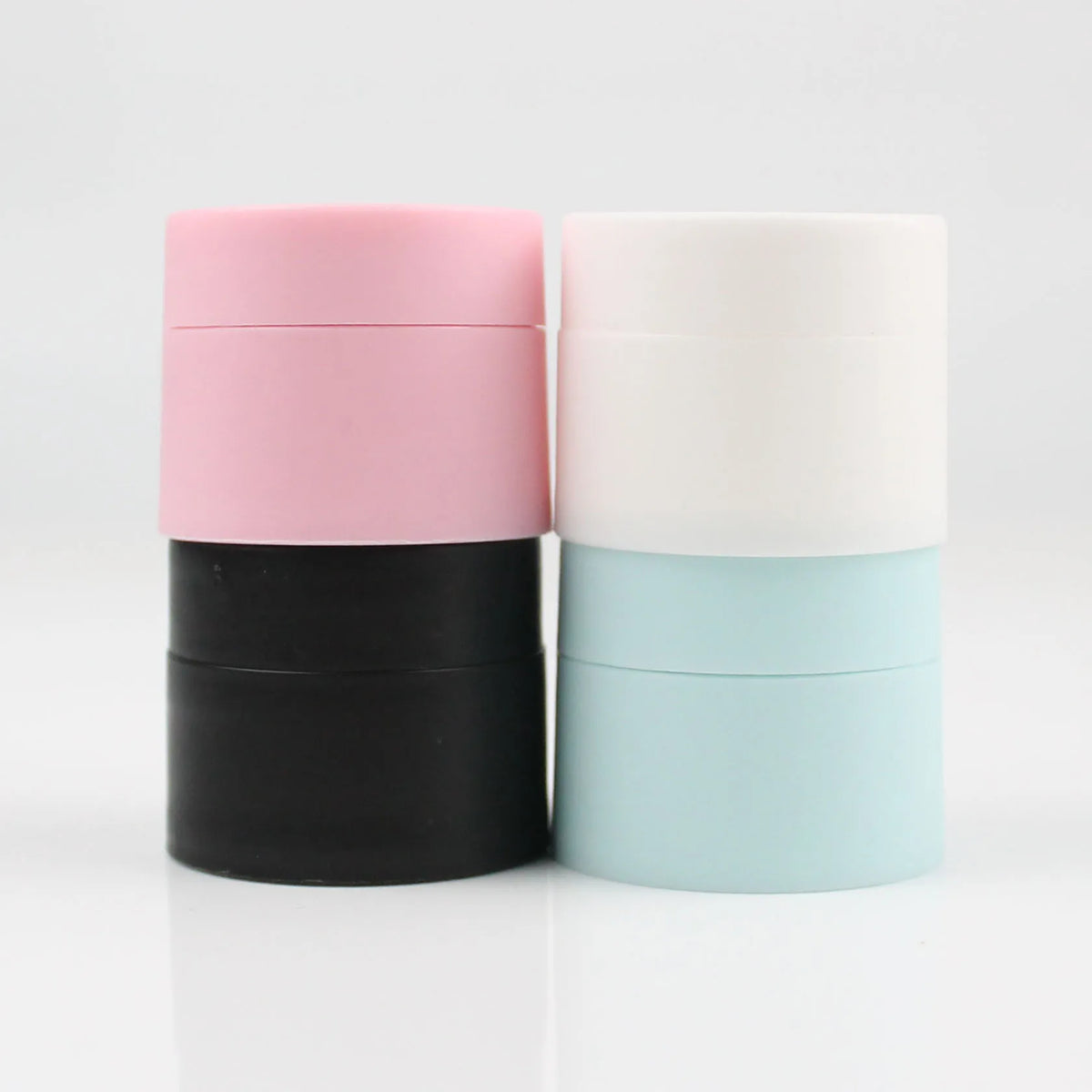 Three refillable travel face cream jars in pink, white, and light blue with leak-proof lids.
