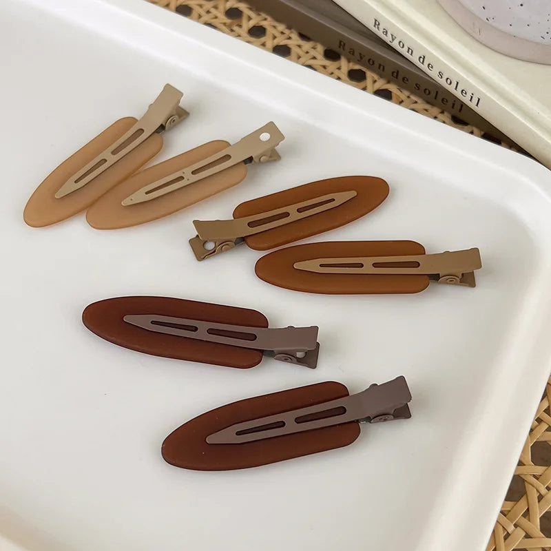 A set of two matte resin side hair clips in various shades of brown and tan are displayed on a white tray.