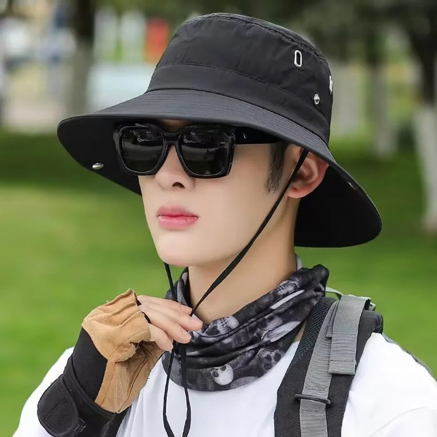 A male model wearing a black UV protection bucket hat and sunglasses outdoors.