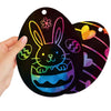 A hand holds a black oval scratch art design of an Easter bunny face and eggs on a dark background.