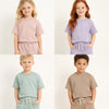 Three children models wearing pastel colored summer tracksuit sets with short sleeves and shorts