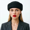 A woman wearing a black knitted beanie and a gray blazer looking directly at the camera.