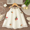 A white sleeveless dress for baby girls with floral embroidery and a delicate lace trim, displayed on a wooden surface.
