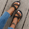 A close-up of women's brown and black breathable mesh flat sandals worn on a foot against a wooden surface.