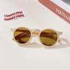 A pair of light beige sunglasses with amber lenses resting on a white surface.