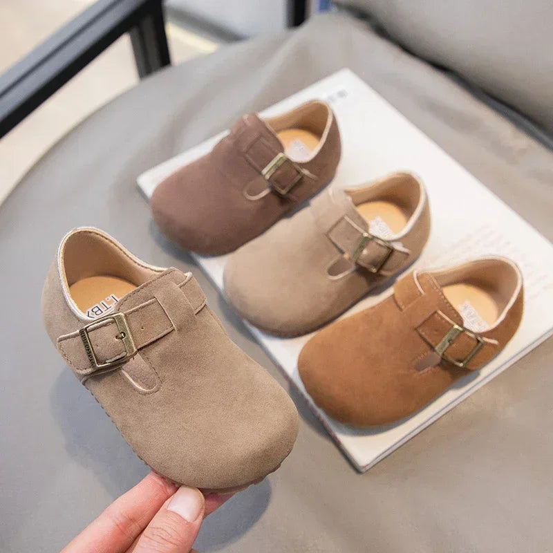 A pair of tan suede kids' moccasin shoes with brown hook-and-loop closures displayed on a light background.