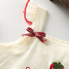 A cream-colored kids summer pinafore dress with red trim and strawberry and bunny print details.
