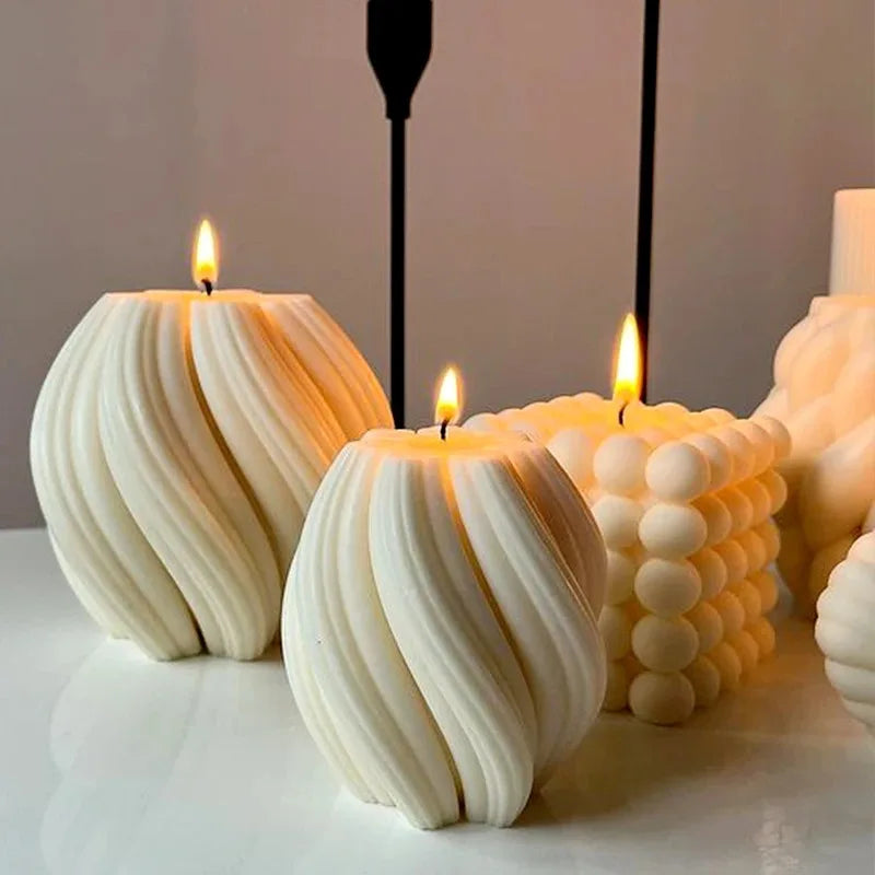 A white pillar candle with a wavy, geometric design is lit on a white surface.