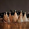 Eine Reihe weißer Silikon-Weihnachtsbaumformen für Kerzen und Gipsarbeiten, beleuchtet mit Kerzen auf einer Holzoberfläche.
