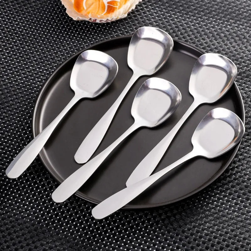 A set of five stainless steel serving spoons arranged on a dark plate and black textured surface.