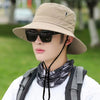 A close-up of a person wearing a beige wide brim bucket hat and sunglasses outdoors.