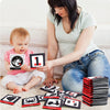 A woman is holding a stack of black and red flash cards featuring letters, numbers, and symbols for baby learning.